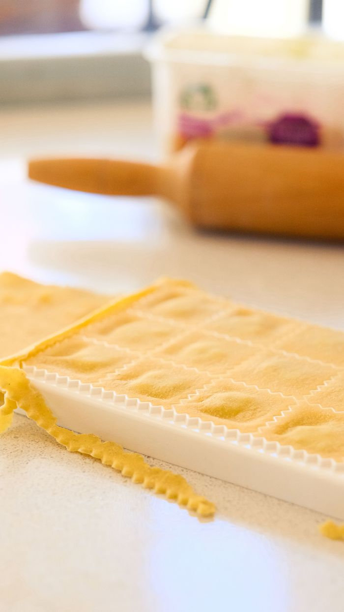 Close-up of homemade ravioli being prepared with a pasta board and rolling pin.