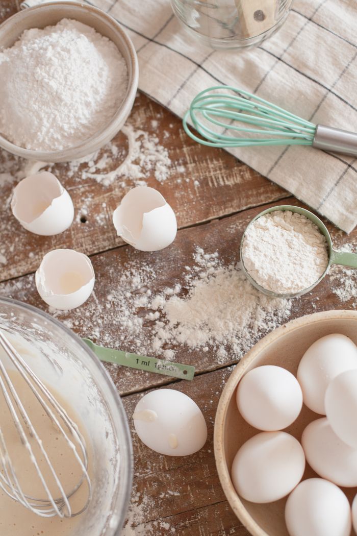 Flat lay of baking essentials including eggs, flour, and utensils on a rustic wooden surface.